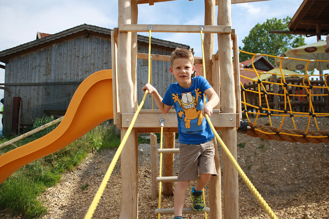 kleines Kind auf einer Kletterleiter auf dem großen Spielplatz hinter der urigen Käsalm in Schönegg