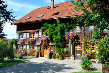 alter uriger Bauernhof mit vielen bunten Blumen an der Hauswand entlang