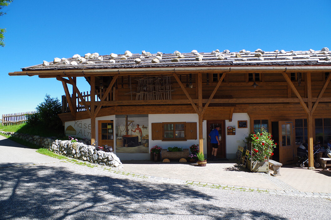 Frontansicht einer urigen Käse-Alm mit Tenne auf einem gekiesten Platz in Schönegg 