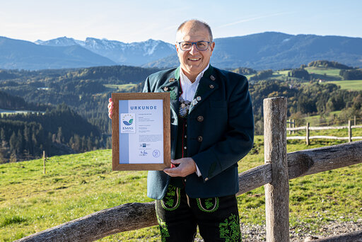 Urkunde der EMAS-Zertifizierung mit Firmeninhaber und Blick in wunderschöne Berglandschaft