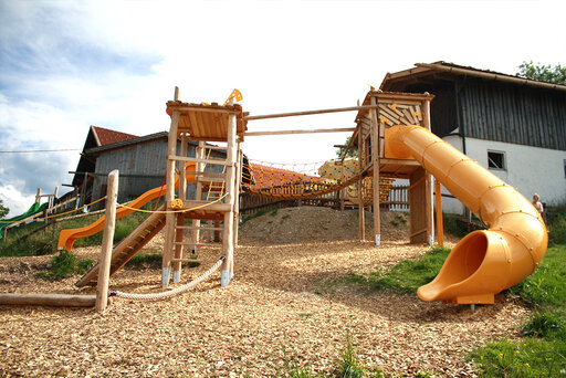 großer Spielplatz im Pfaffenwinkel mit einer Rutsche in einer Käseform, einer Schaukel und einem hohen Turm