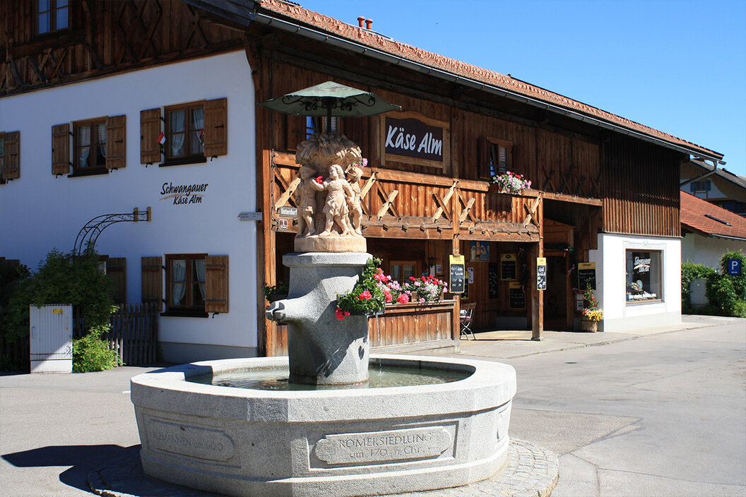 uriger kleiner Käseladen mit einer Holzfassade in Schwangau hinter dem Dorfbrunnen