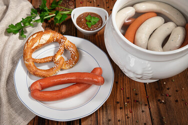 leckere Weißwürste und Käswürste in einem Keramiktopf serviert mit einer bayerischen Breze