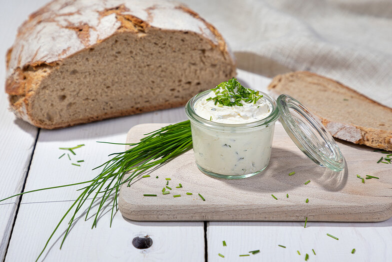 cremiger, feiner Frischkäse mit knusprigem Bauernbrot aus Sauerteig verziert mit Schnittlauch und Holzbrett