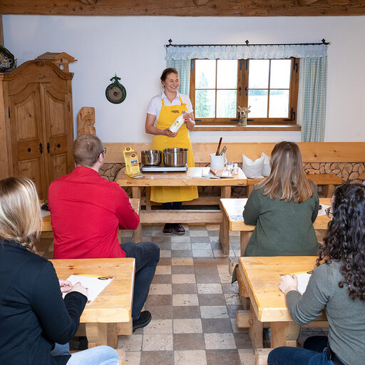 eine kleine Personengruppe sitzt im Käsekurs und hört aufmerksam der Käsermeisterin zu die vieles rund um den Käse erzählt