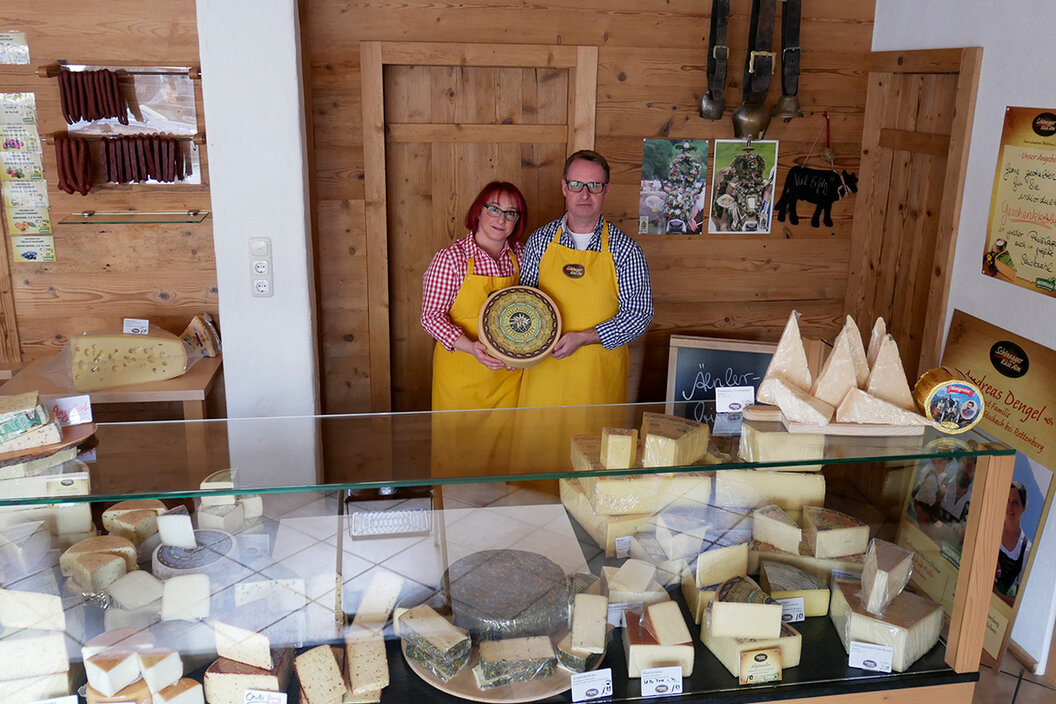 Besitzer der Käse-Alm in Immenstadt hinter der Käsetheke die mit vielen verschiedenen Käsespezialitäten gefüllt ist