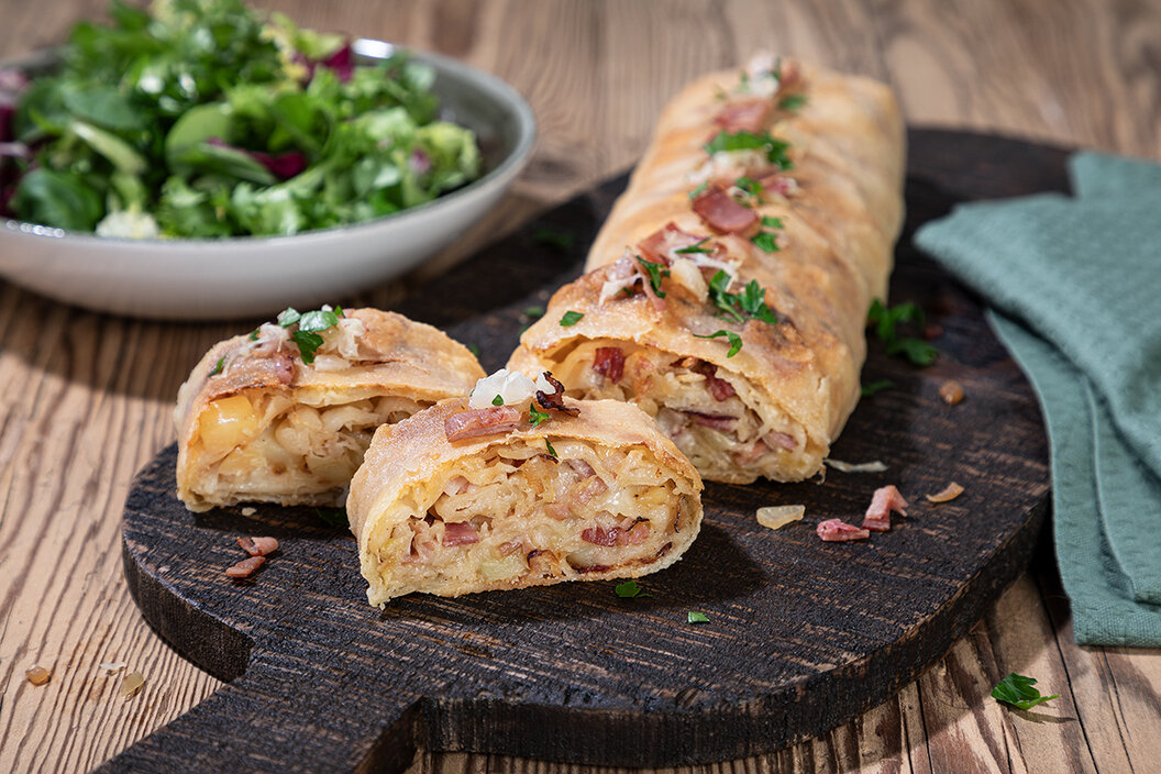 Herzhaften Strudel selber machen. Leckerer Käse Kraut Strudel verfeinert mit Speckwürfel. Garniert mit Kräutern.
